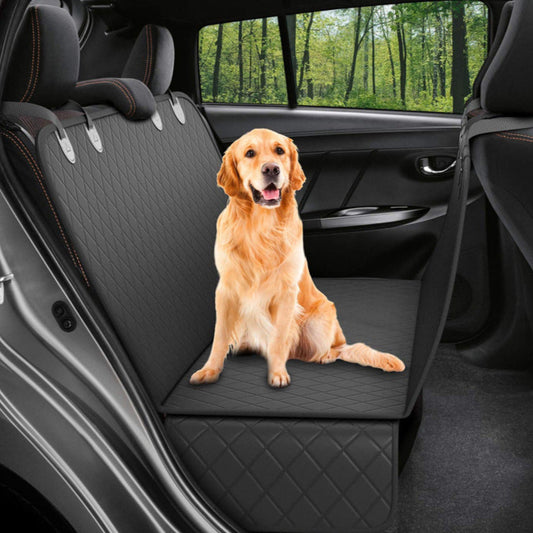 Dog sitting on a black car seat cover in a vehicle with greenery outside.