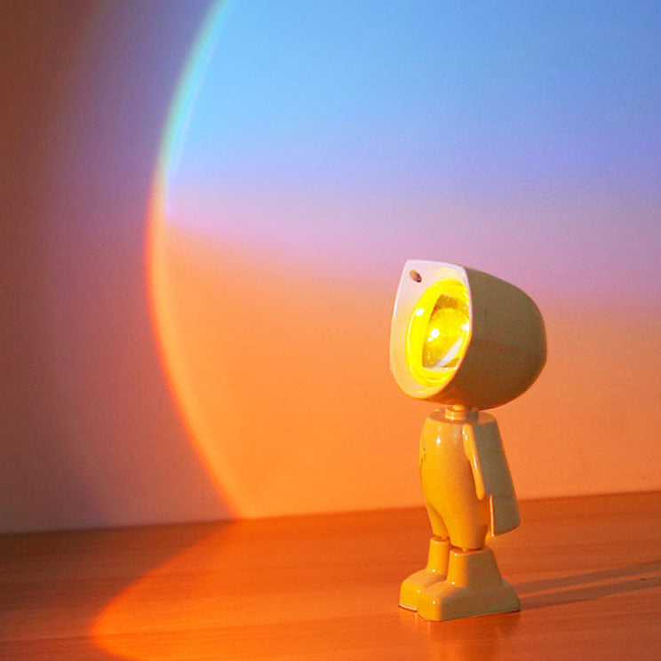 A mini robot sunset projector light with a light on a wooden surface with a colorful gradient background