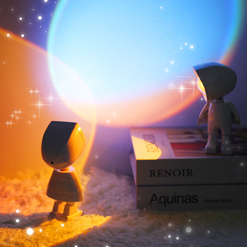 Two mini robot sunset projector lights standing on books with a colorful, starry background
