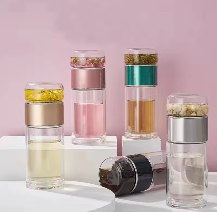 Set of glass tea infuser bottles with different colored layers on a pink background