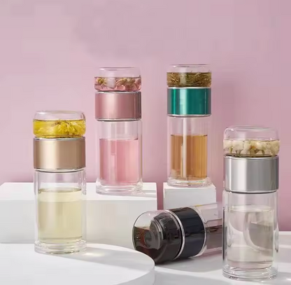 Set of glass tea infuser bottles with different colored layers on a pink background