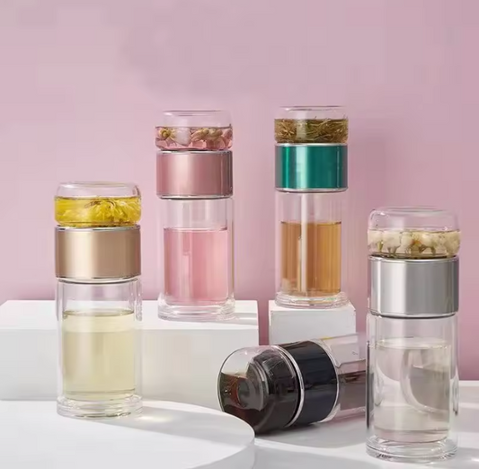 Set of glass tea infuser bottles with different colored layers on a pink background